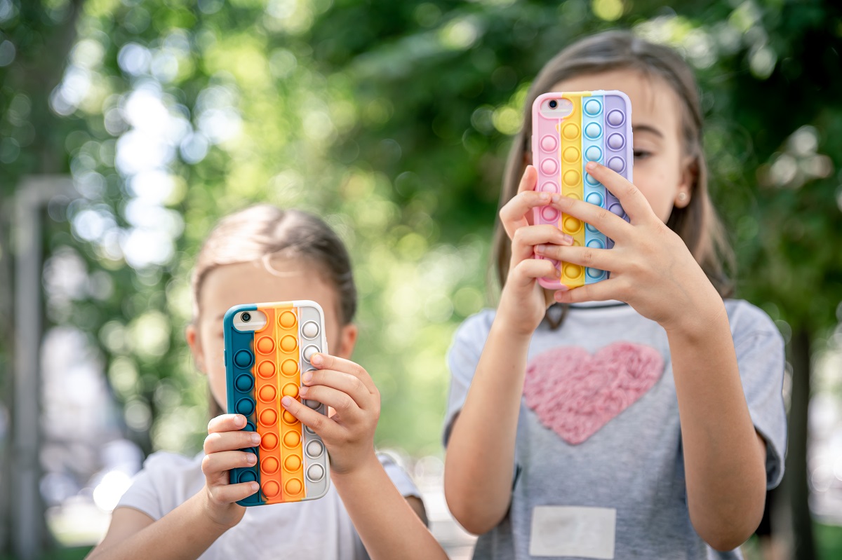 Little girls use phones in trendy cases for anti stress pop it.